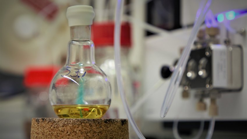 A flask with a yellowish oil in foreground, an HPLC pump in the background.